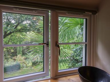 A window overlooking a garden with trees and plants at The Bothy at Lewis Cottage Spreyton