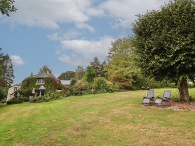 An outdoor photo of a house and lawn with chairs at The Bothy at Lewis Cottage Spreyton