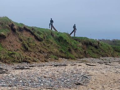 Two statues on a grassy hill at the beach