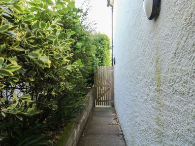 A pathway next to a wall with bushes and a gate at Lorrell in Salcombe