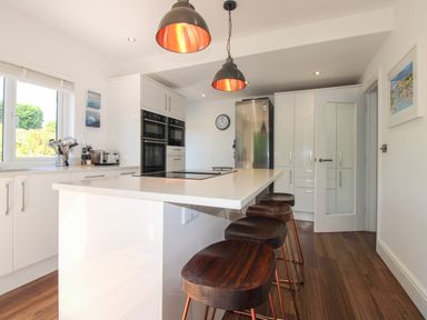 A kitchen with a countertop island and bar stools at Lorrell in Salcombe