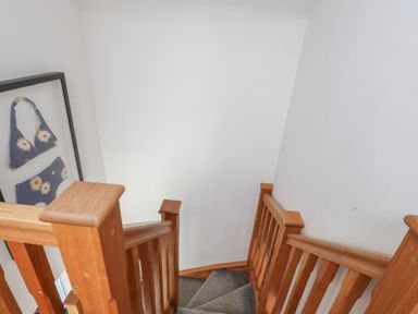 A staircase with wooden railing and framed artwork at Kiloran in Rhosneigr