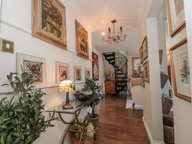 A hallway with paintings on the wall and a staircase at 7 The Cedars Wotton-Under-Edge