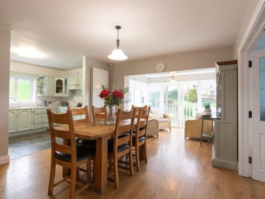 A dining room with a table and chairs leading to a sunroom at An Grianan Getaway Burt