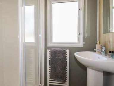 A bathroom with a shower, sink, and window at Shamrocks Cove Caravan