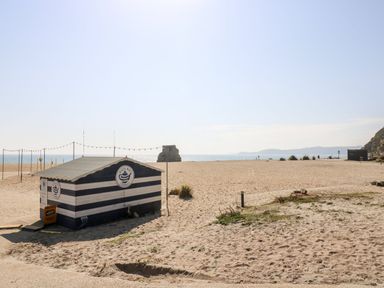 A beach with a striped hut and ocean view at Farthings, The Old Chapel, St Austell