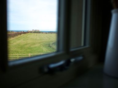 A view of a castle and grassland from a window at The Chimney in Bamburgh