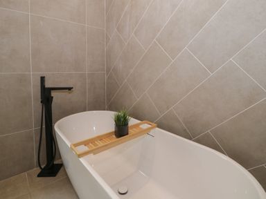 A bathroom featuring a bathtub with a wooden tray and plant at Llety Cllyd in Barmouth