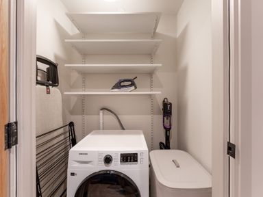A laundry room with a washing machine, ironing board, and vacuum cleaner at Hidden 1- Clifftop House Hot Tub, St Ives
