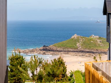 A view of the beach and hillside with water and a lighthouse at Hidden 18- St Ives Bay Suite Hot Tub, St Ives