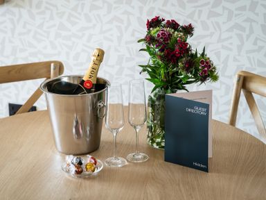 A dining table with a champagne bottle, glasses, flowers, and guest directory at Hidden 10- Godrevy View St Ives