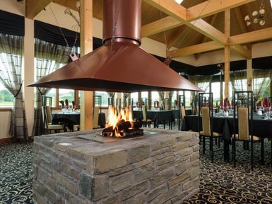 A restaurant with a central fireplace and dining tables at Sidlaw, Fowlis near Dundee