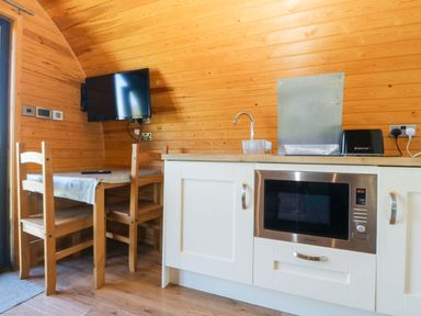 A kitchen with a microwave, sink, dining table and chairs at Bron Eifion Pod 1 Criccieth