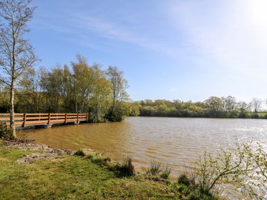 A body of water with a wooden bridge and trees at Bron Eifion Pod 1 Criccieth