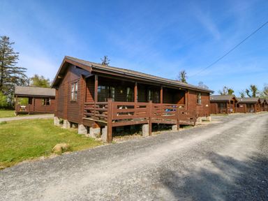 A log cabin with a deck and parking area at Lodge 2 -  Bron Eifion