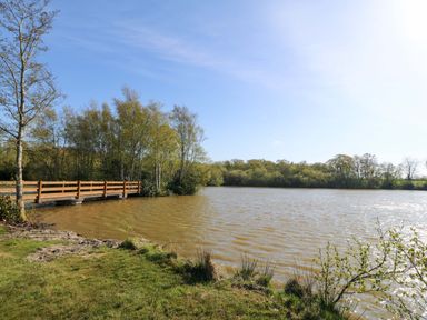 A view of a lake with a wooden bridge and trees at Lodge 2 -  Bron Eifion