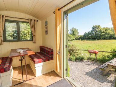 A dining area with a table and benches overlooking a garden at The Three Spaniels Shepherds Hut in Cwrtnewydd near Llanybydder