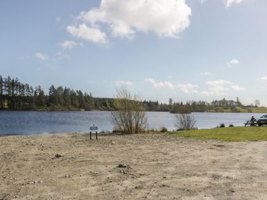 A lake with trees and a bench at Standard Caravan at Three Lochs Holiday Park in Newton Stewart