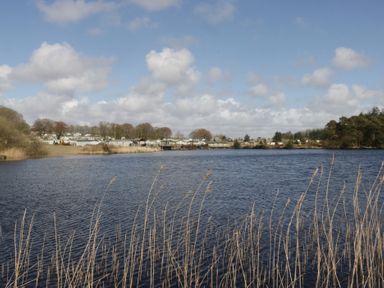 A view of a lake with caravans and trees at Lochwood Platinum Superior at Three Lochs Holiday Park Newton Stewart