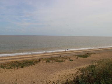 A beach with people walking along the shoreline at The Mill House Gardens