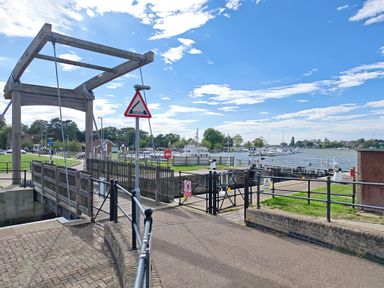 A wooden bridge structure and boats on a waterway at The Mill House Gardens Oulton Broad