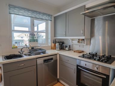 A kitchen with a sink, dishwasher, stove, and kettle at 2 Lyme Mews Seaton