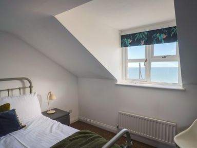 A bedroom with a bed and window overlooking the sea at 2 Lyme Mews in Seaton