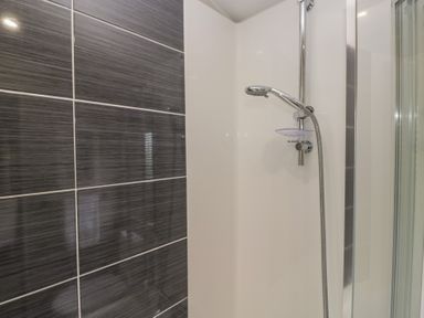 A shower with a showerhead and wall tiles at Swan Haven in Grange-Over-Sands