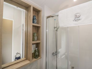 A bathroom with a shower, mirror, and shelf at Swan Haven in Grange-Over-Sands