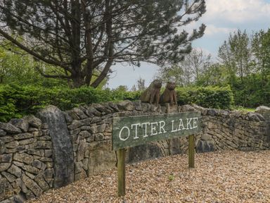 A sign for Otter Lake beside stone wall and sculptures at Swan Haven in Grange-Over-Sands