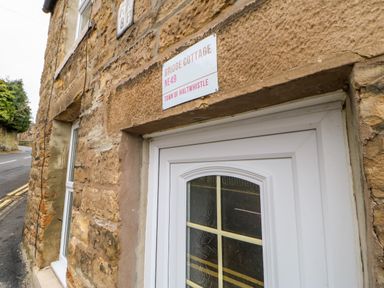 A stone building with a white door and a sign reading Bridge Cottage NE49 Town of Haltwhistle