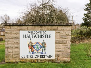 A welcome sign for Haltwhistle centre of Britain mounted on a stone wall outdoors