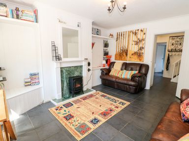 A living room with two brown leather sofas a fireplace with a mirror above a colorful rug and a wall painting at Bridge Cottage Haltwhistle near Hadrians Wall