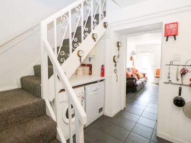 A staircase with carpet and a laundry area with washing machine and dishwasher underneath the stairs leading into a living room with a sofa at Bridge Cottage in Haltwhistle near Hadrians Wall