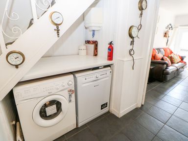 A laundry area under stairs with a washing machine and dishwasher near a living room at Bridge Cottage in Haltwhistle near Hadrian's Wall