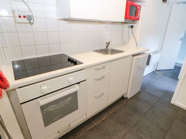 A kitchen with an oven stovetop sink small refrigerator and a red microwave at Bridge Cottage in Haltwhistle near Hadrians Wall