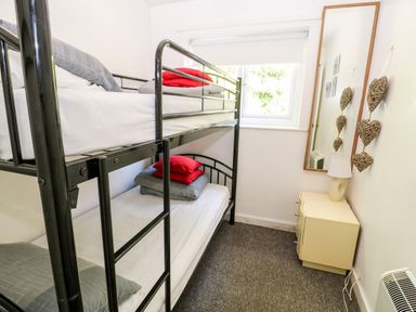 A small bedroom with a black metal bunk bed a cream bedside table with a lamp and a wall mirror at Bridge Cottage Haltwhistle near Hadrians Wall