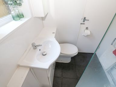 A small bathroom with a sink, toilet, window with glass vases with plants, and a towel on a rail at Bridge Cottage in Haltwhistle near Hadrians Wall