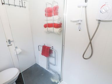 A bathroom with a toilet shower showerhead towel racks with red and white towels at Bridge Cottage Haltwhistle near Hadrians Wall