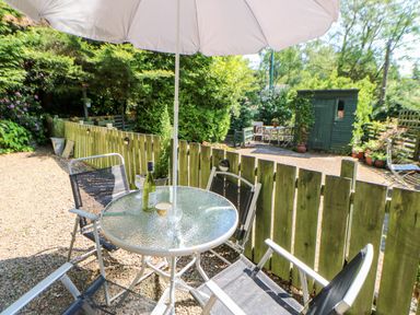 An outdoor patio area with a round glass table and four chairs under a white umbrella a fence and garden shed in the background at Bridge Cottage in Haltwhistle near Hadrians Wall