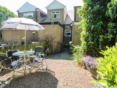 An outdoor patio area with a table, chairs, and umbrella next to a house with plants and flowers at Bridge Cottage in Haltwhistle near Hadrian's Wall