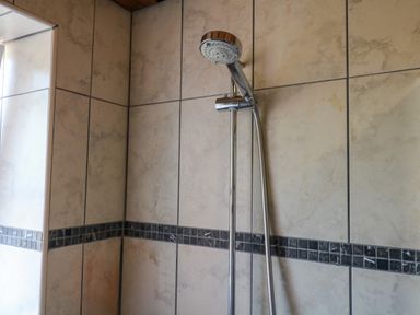 A shower head and wall tiles in the bathroom at Gorway Cottage Teignmouth