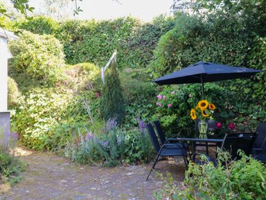 A garden with a table and chairs under an umbrella at Gorway Cottage in Teignmouth