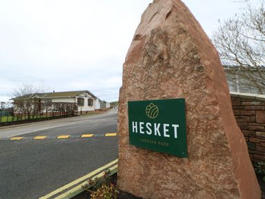 A sign for Hesket Caravan Park with a building in the background