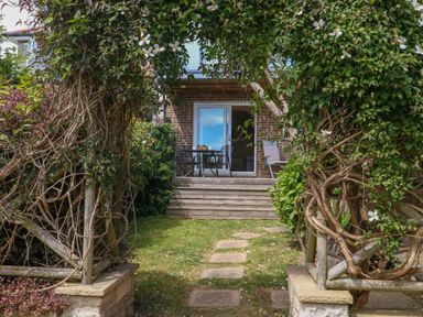 A garden with a pathway leading to a patio area at Little Gem in Weymouth