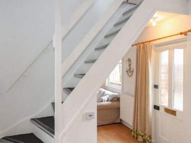 A hallway with a staircase and a front door at Pixie Cottage in Weymouth