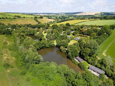 An outdoor area with a lake and houses surrounded by trees at 11 Water's Edge near Pelynt