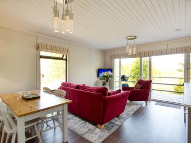 A living room with a sofa, armchair, dining table and television at 2 bedroom lodge with stunning loch, mountain views Crianlarich