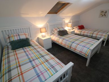 A bedroom with three beds and a lamp on a nightstand at The Cartwheel in Amroth