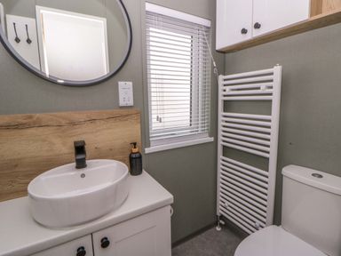 A bathroom with a sink, mirror, toilet, and radiator at The Dorchester at Bay View in New Quay